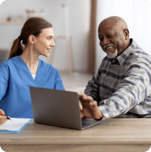 Healthcare worker assisting elderly man with laptop.
